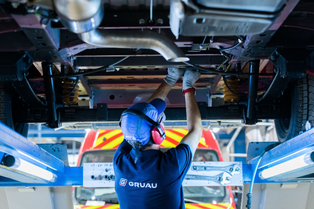 Technicien de maintenance portant ses EPI (casque antibruit et gants) pour intervenir en toute sécurité sous un véhicule sur un pont élévateur.